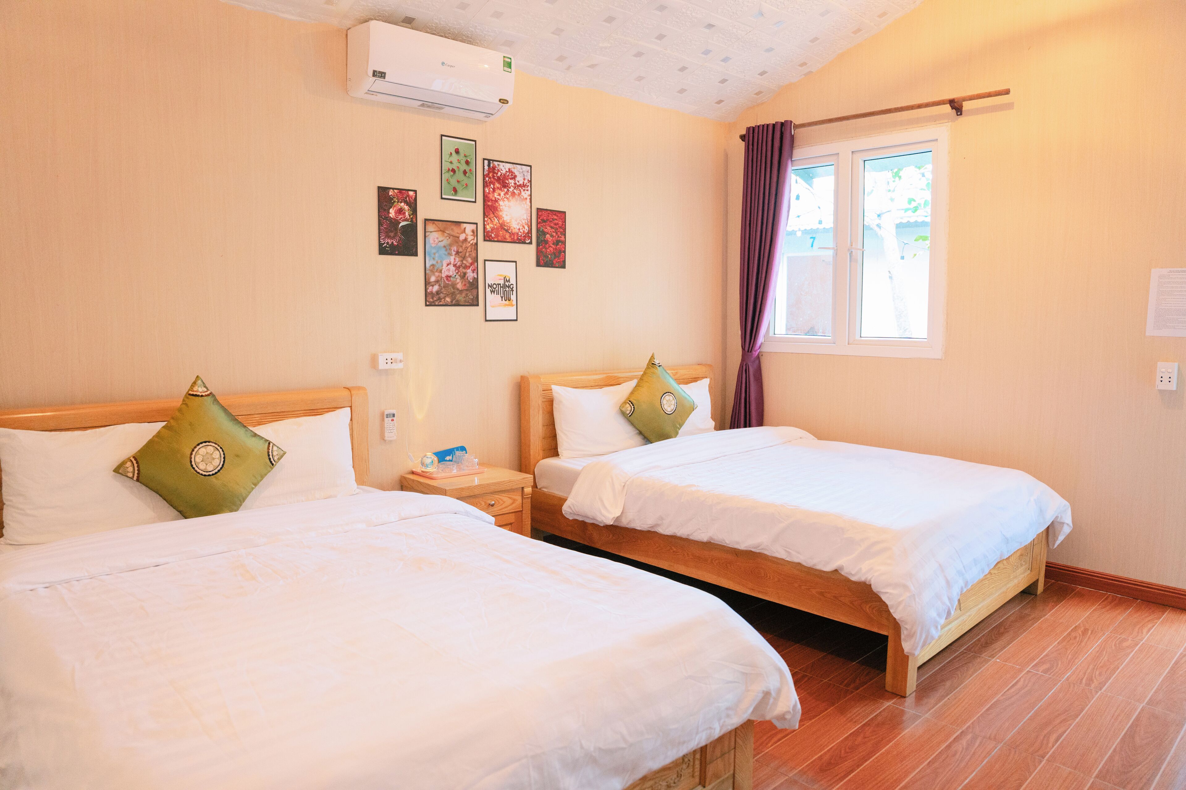 Une chambre d’hôtel avec deux lits, une fenêtre avec des rideaux et plusieurs tableaux encadrés accrochés au mur.