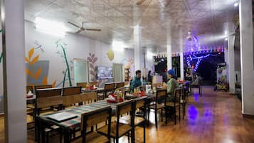 Restaurante com mesas e cadeiras de madeira, um ventilador de teto e decorações nas paredes, incluindo uma libélula e bambu.
