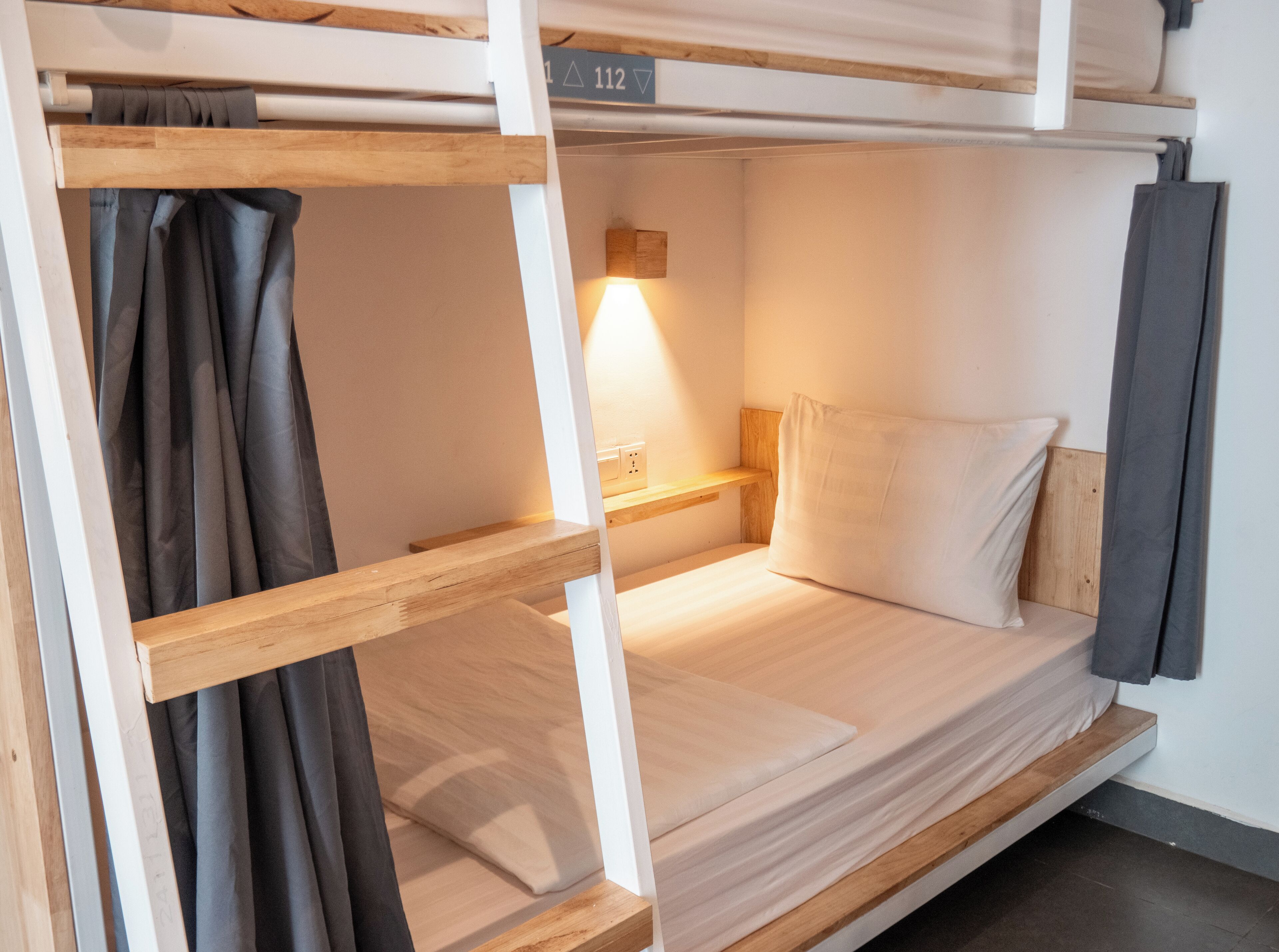 A bunk bed with a wooden frame, a bedside table with a lamp, and a curtain.
