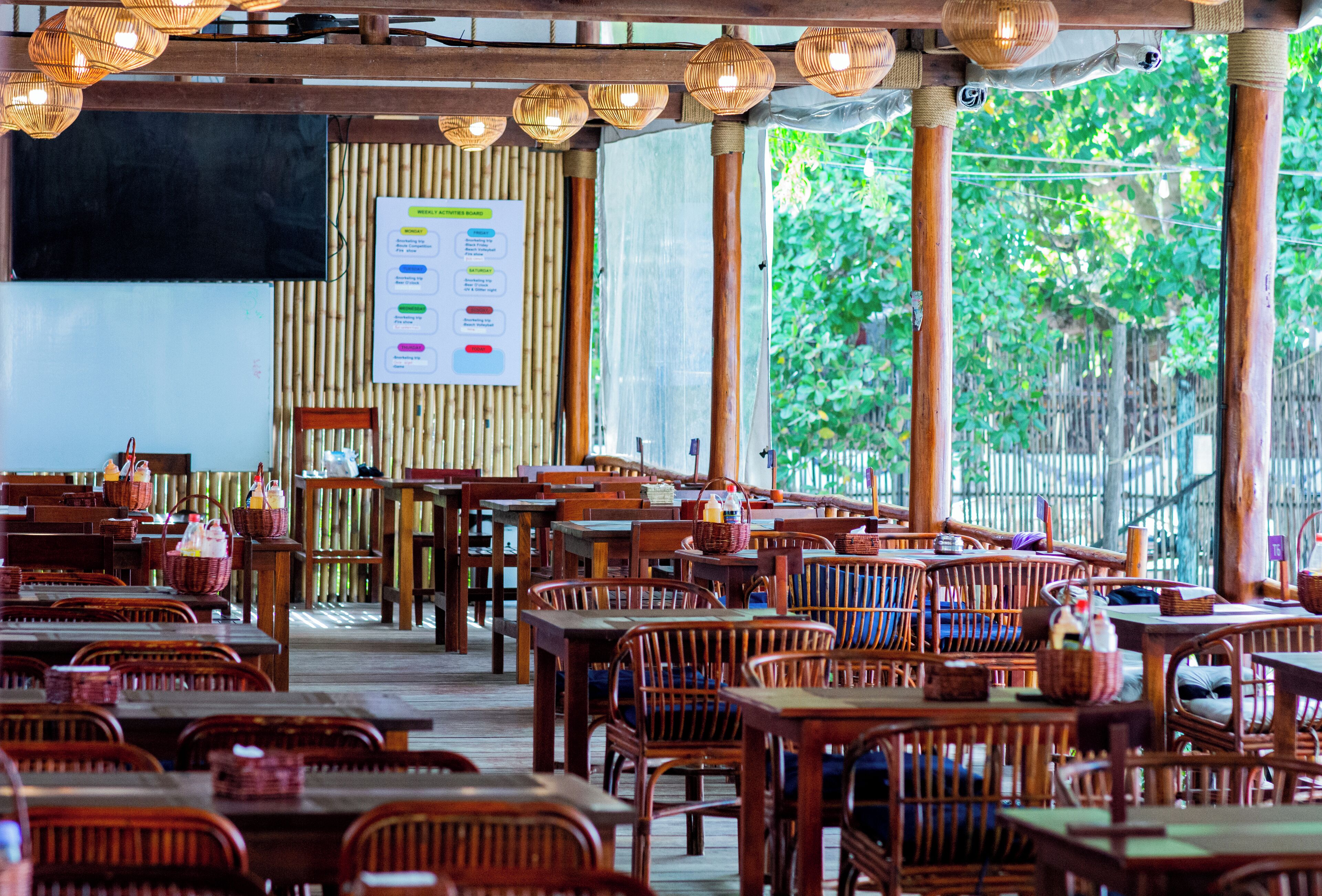 Un restaurant intérieur avec des tables et des chaises en bois, des cloisons en bambou et des luminaires suspendus.