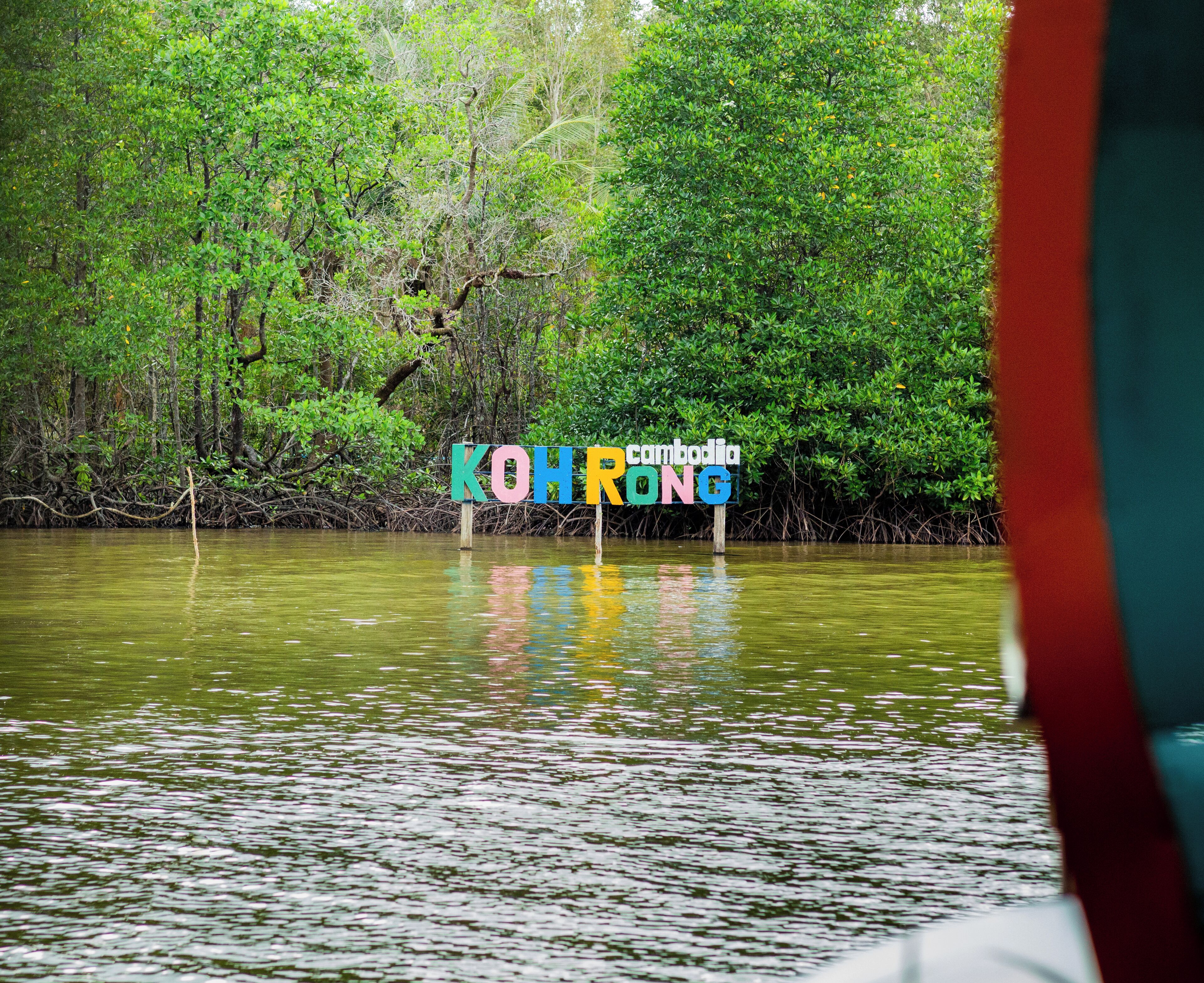 A sign with the text "KOHROONG Cambodia" in a mangrove setting.