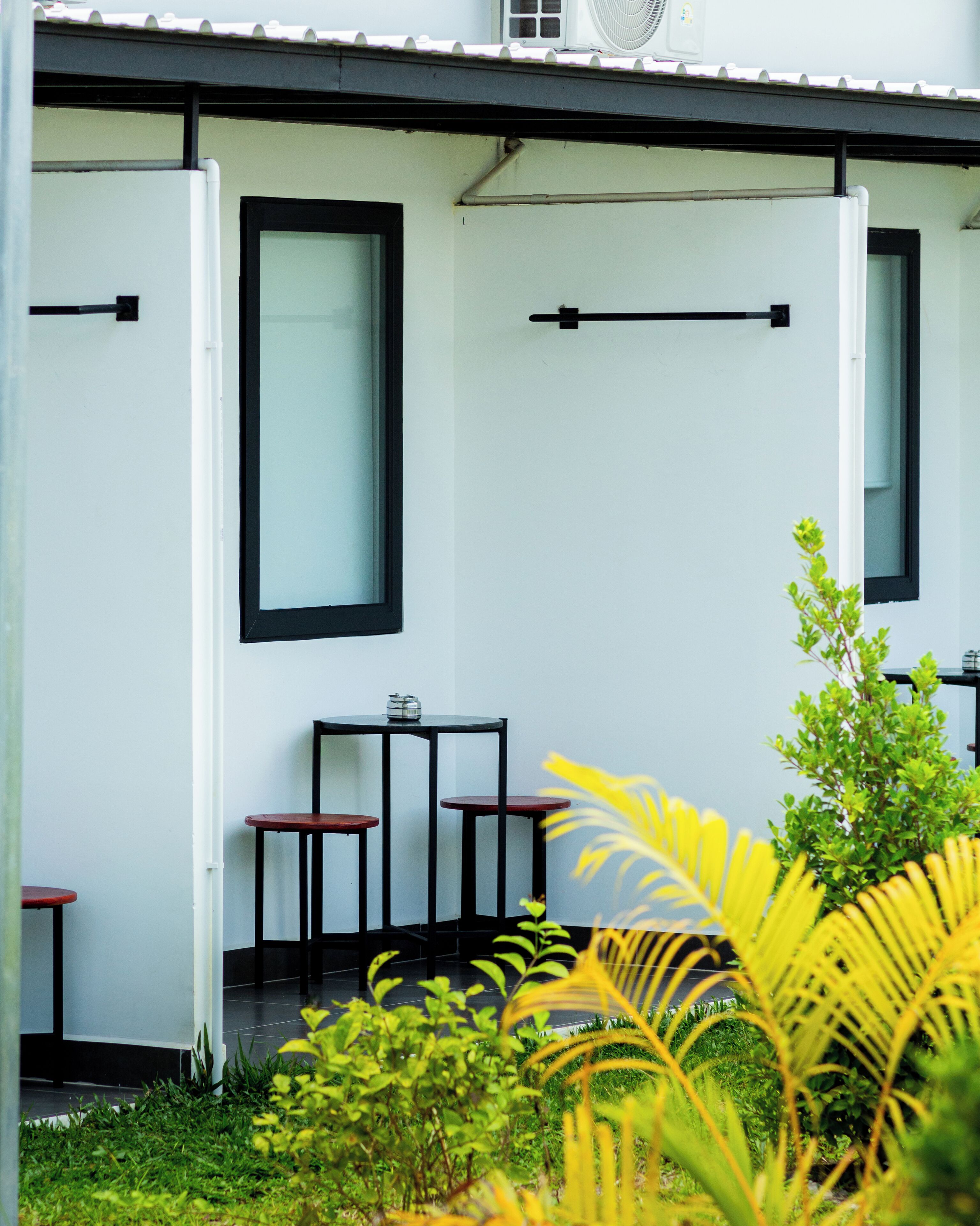 A building with a white exterior, black-framed windows, and a small outdoor seating area with tables and chairs.