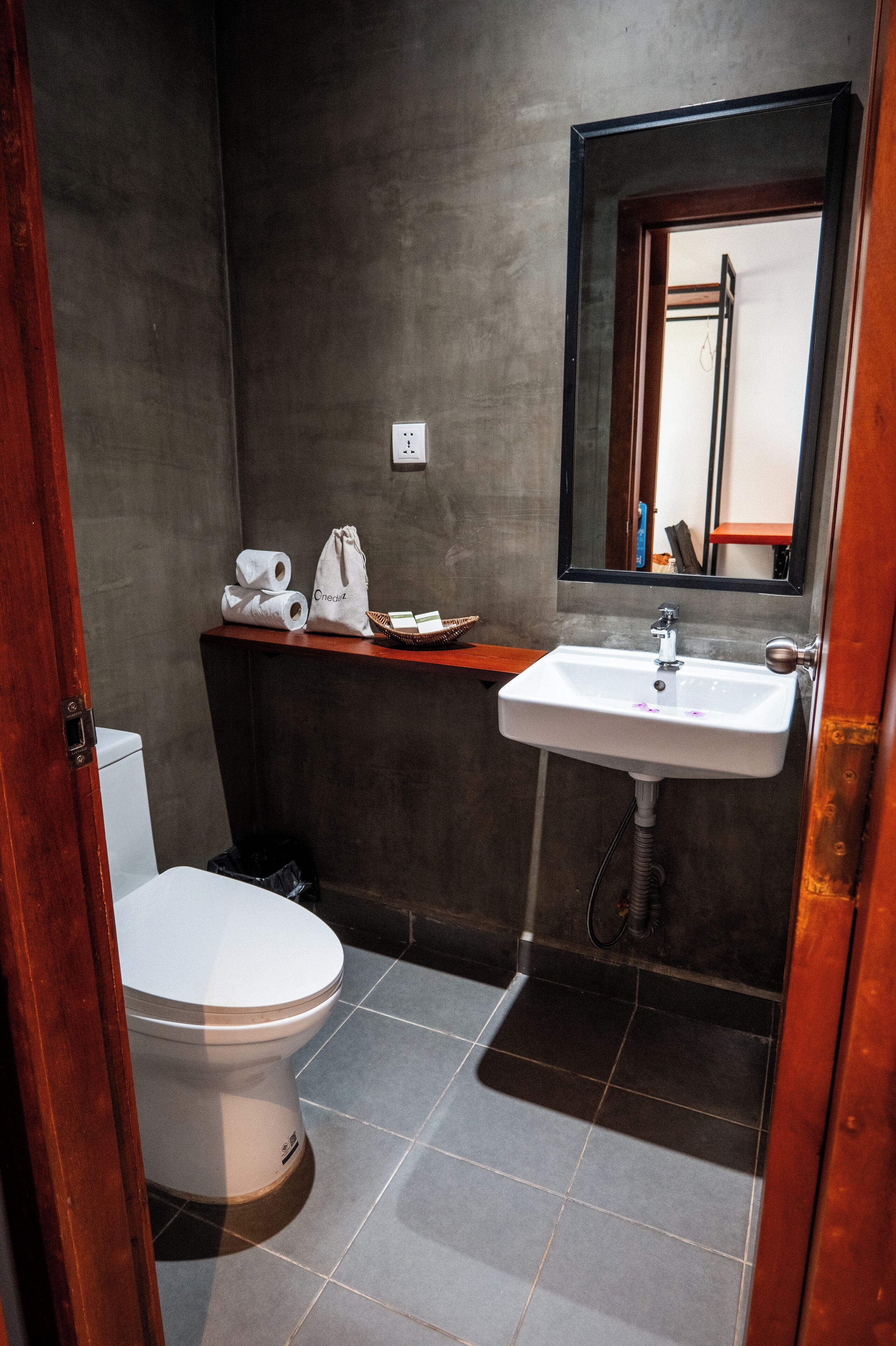 A compact bathroom with a white toilet, a sink with a mirror above it, and a shelf with towels and toiletries.