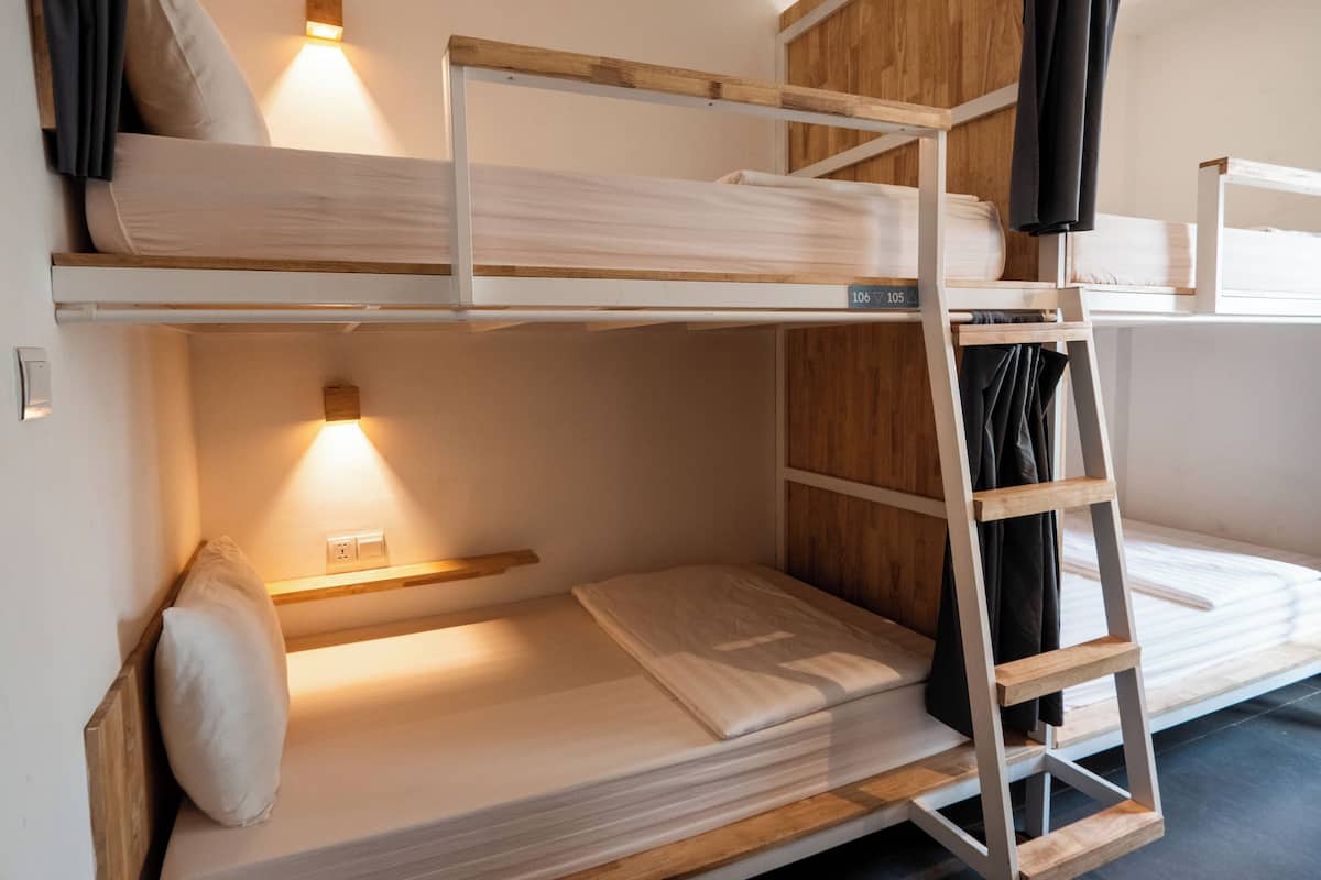 Habitación con literas, una escalera de madera, estante y una lámpara fijada a la pared.