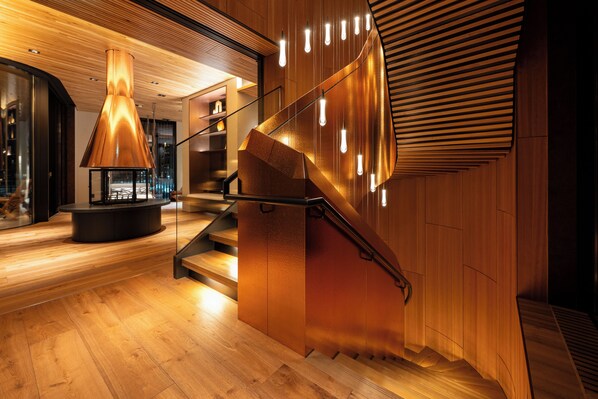 Un interior moderno con una escalera de madera, un elemento de iluminación central y un diseño de pared curva.