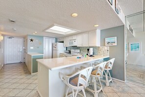 A kitchen with a central island, white bar stools, and a microwave. - Gulf-Front 2BR w/ Balcony: Suntide III - Unit 502 (South Padre Island)