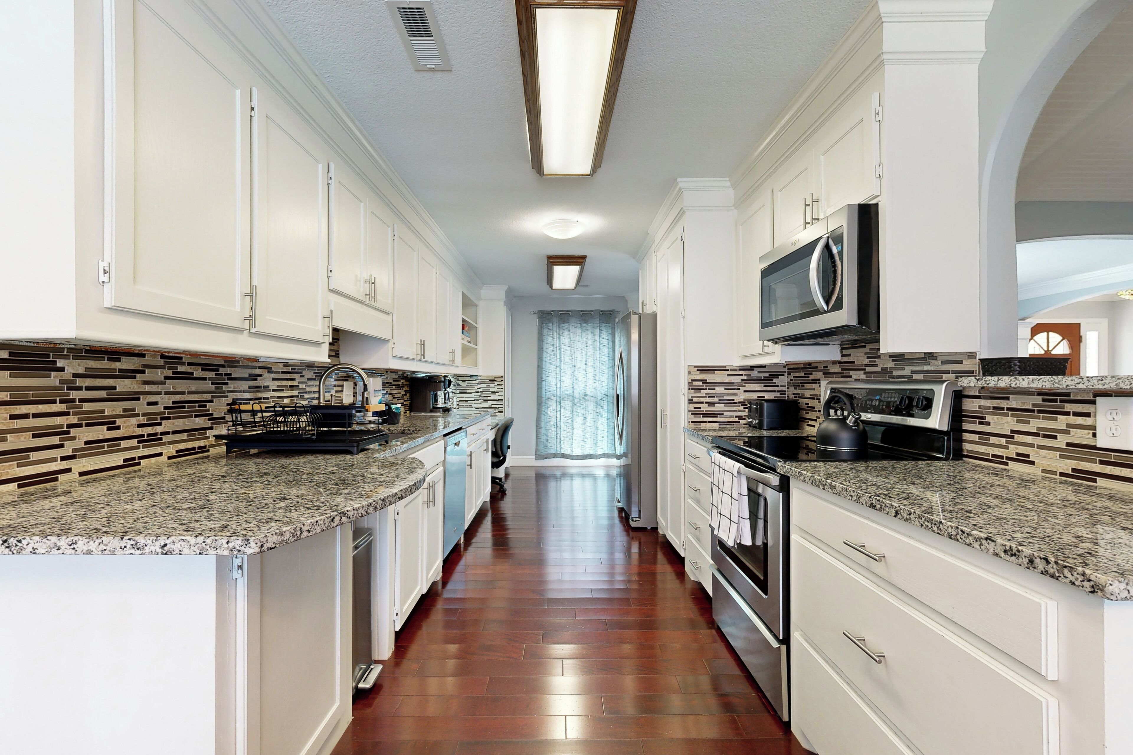 A kitchen with white cabinets, granite countertops, and a tiled backsplash.