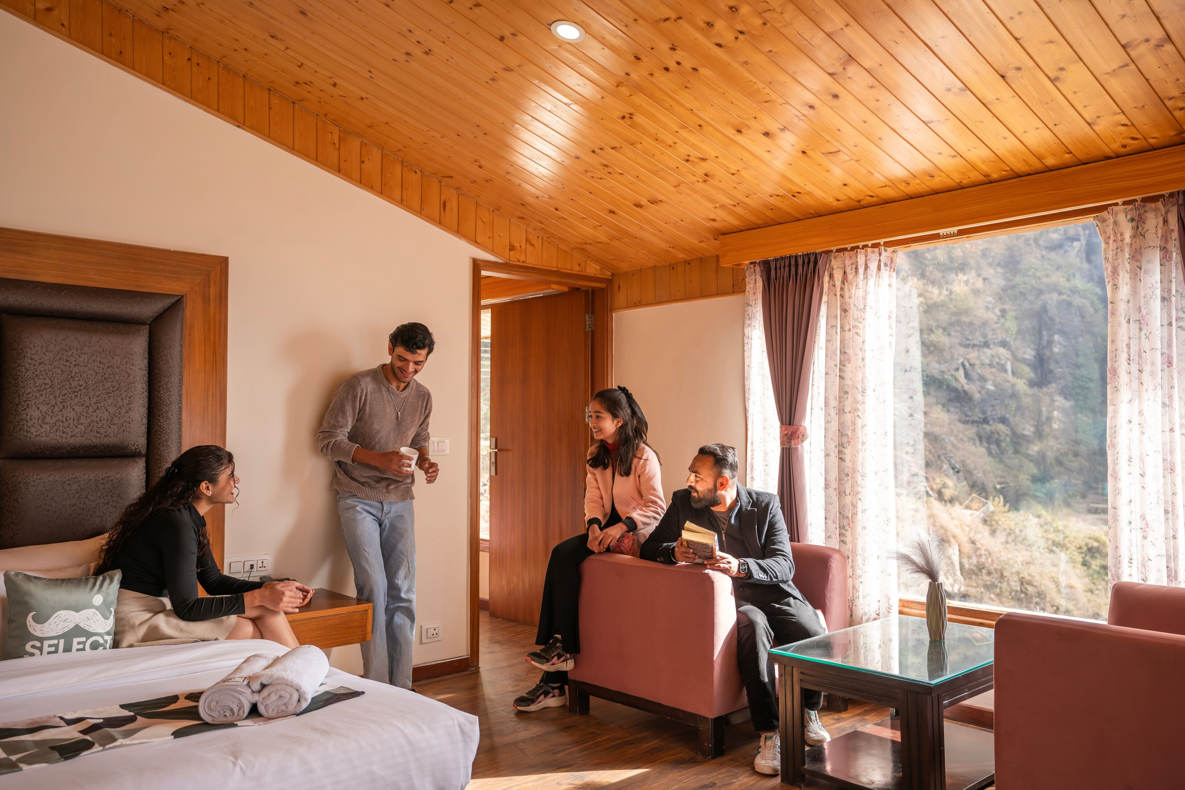 Una habitación con techo de madera, una cama con almohada, una mesa de vidrio y vistas a un paisaje montañoso a través de la ventana.