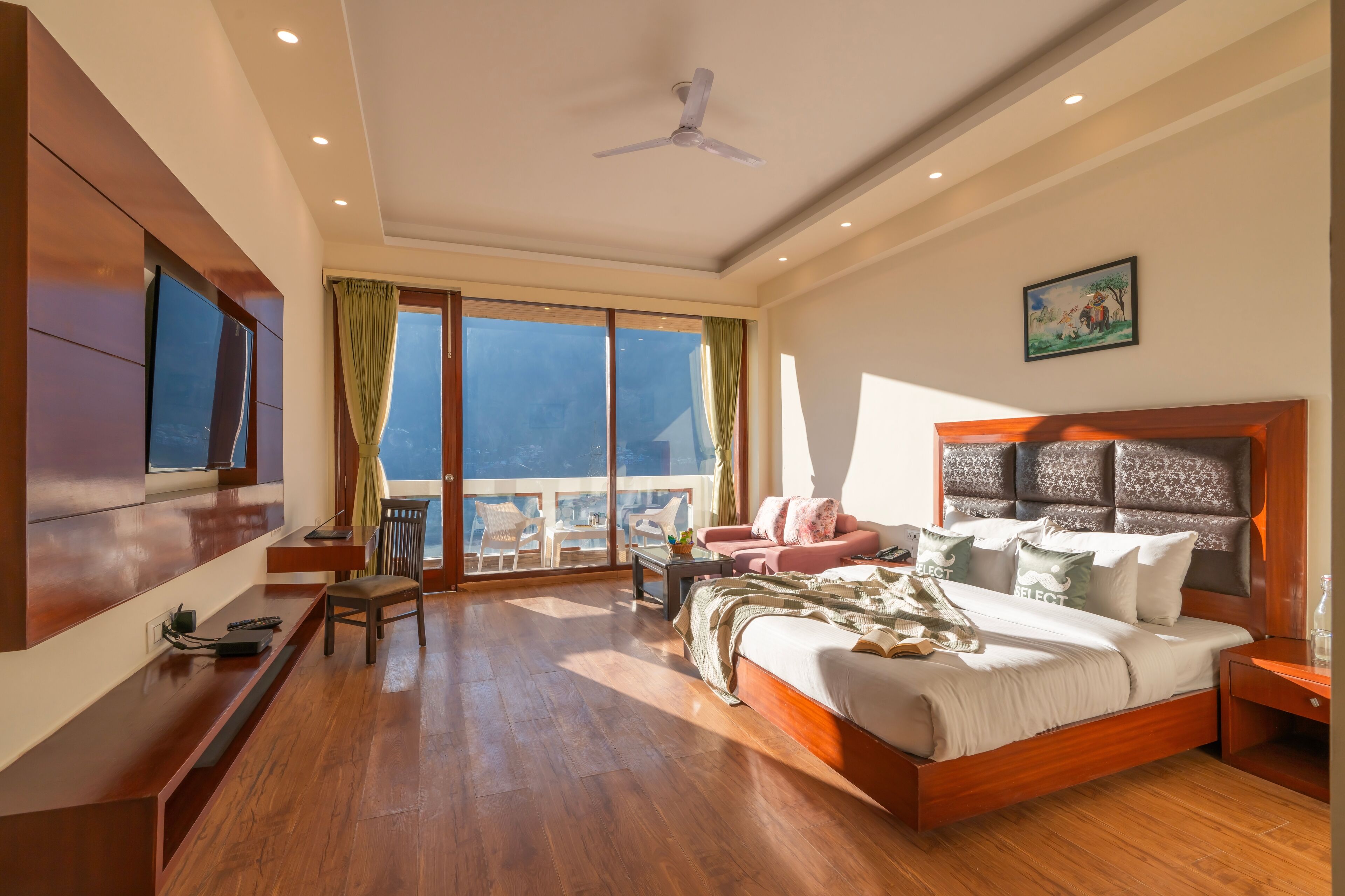 A spacious bedroom with a large bed, a desk, and a balcony with a view.