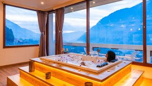 A modern bathroom with a large bathtub, wooden bench seating, and a view of mountains through large windows. - Moustache Select Manali (Manali)