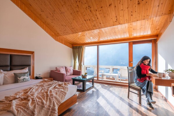 A bedroom with a large bed, a sofa, a coffee table, and a chair. There is a window with a view of the outside. - Moustache Select Manali (Manali)