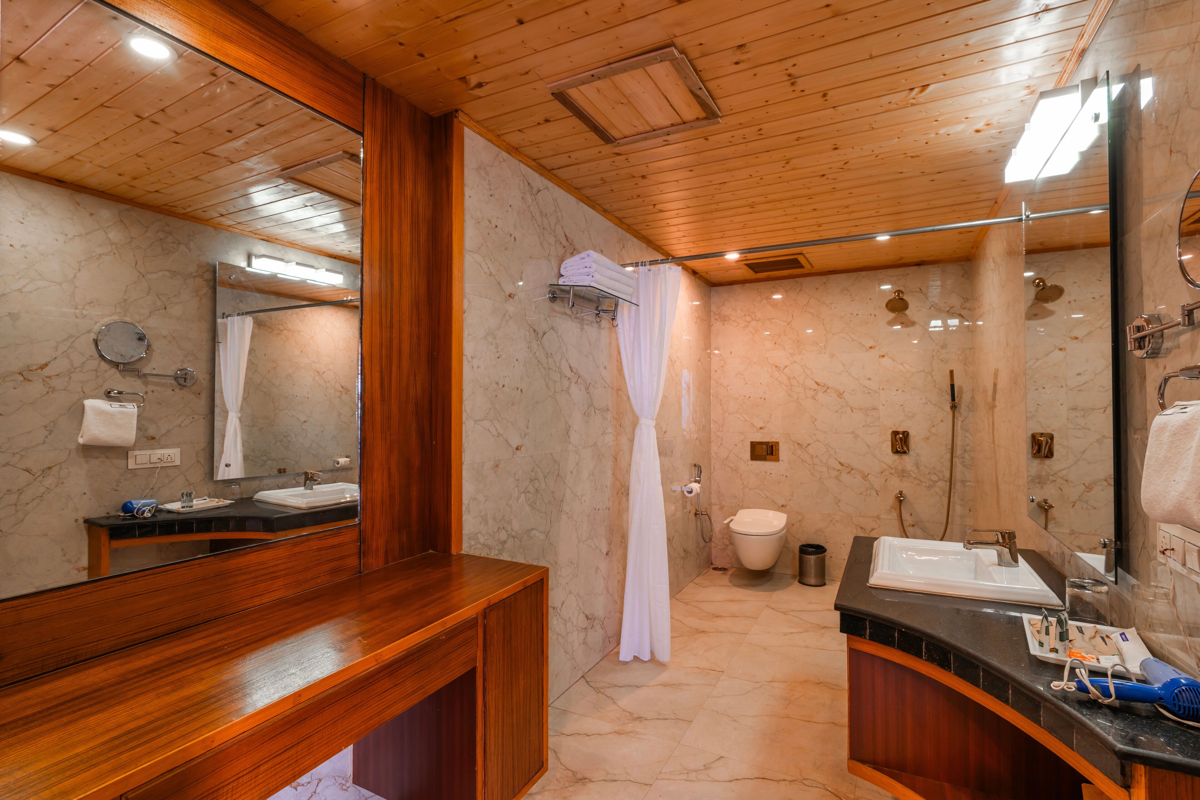 Et moderne badeværelse med træloft, marmorvægge, et stort spejl, en trækommode, et bruseområde og et toilet.