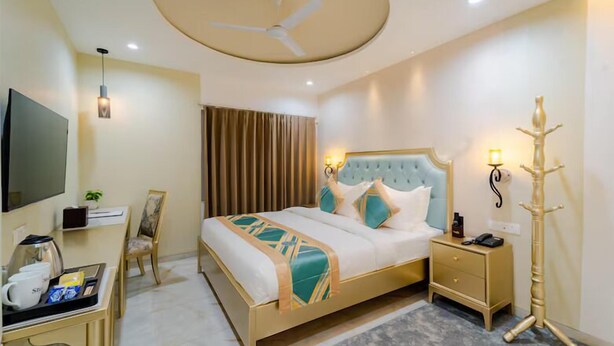 A hotel room with a bed, bedside table, lamp, TV, desk, chair, and a floor lamp. - STUDIO BY JARDIN  (Indore)