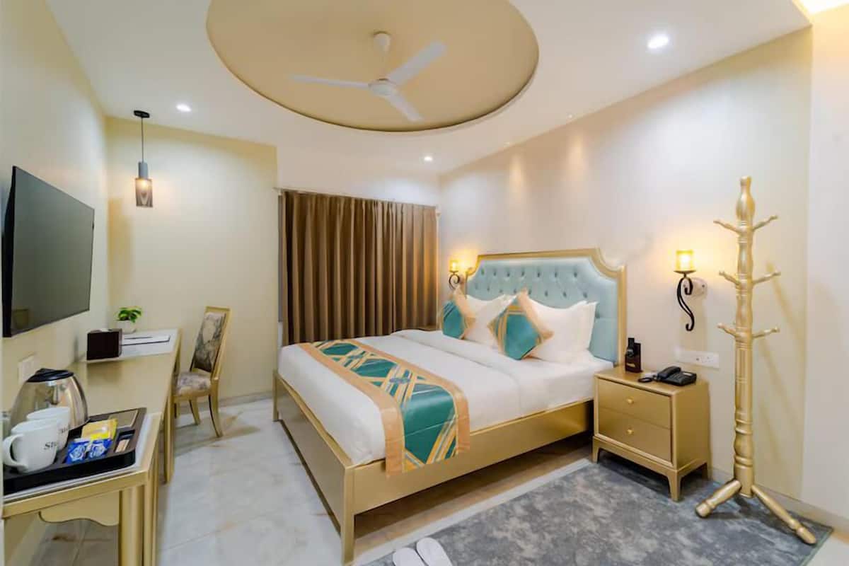 Habitación de hotel con cama, mesita de noche, lámpara, televisor, escritorio, silla y lámpara de pie.