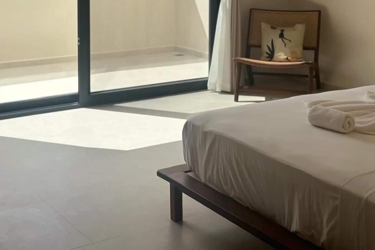Un dormitorio con cama, una silla, una ventana con vistas a vegetación y una puerta corrediza.