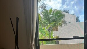 Ein Hotelzimmer mit Bett, weißen Handtüchern, einem Fenster mit Blick auf Palmen und Gebäude.