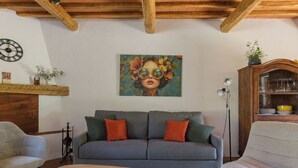 Ein Wohnzimmer mit grauem Sofa, zwei Sesseln, einem Holztisch, einem Gemälde an der Wand und einer Holzvitrine mit Gläsern.