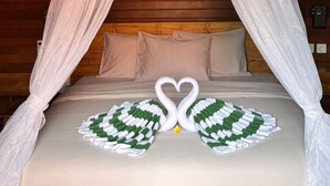 Una cama con dosel, almohadas y un cisne decorativo hecho con toallas.