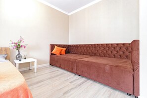 A room with a brown sofa, a small white table, and a vase with flowers.