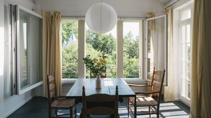 Ein Essbereich mit Tisch, Stühlen, einer Pendelleuchte und großen Fenstern mit Vorhängen.