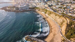 An aerial view of a coastal city with a beach, buildings, and a rocky breakwater. - Quinta Maresia Tiny House 2 (Carvoeira)