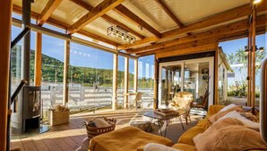 A cozy wooden cabin with a large glass window, a fireplace, and a comfortable seating area with cushions. - Quinta Maresia Tiny House 2 (Carvoeira)