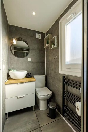 Een moderne badkamer met een wit wastafelmeubel, een ronde spiegel en een toilet.