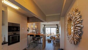 Une cuisine moderne dotée d’appareils électroménagers intégrés, un coin repas avec une table et des chaises en bois, et un grand élément décoratif mural.