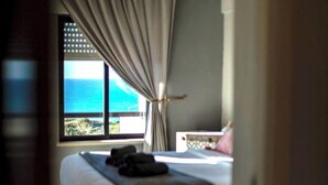 Une chambre à coucher avec un lit, une fenêtre avec des rideaux et une vue sur la mer.