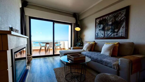 Un salon moderne avec un canapé, une table basse et une vue sur l’océan grâce à de grandes portes coulissantes.