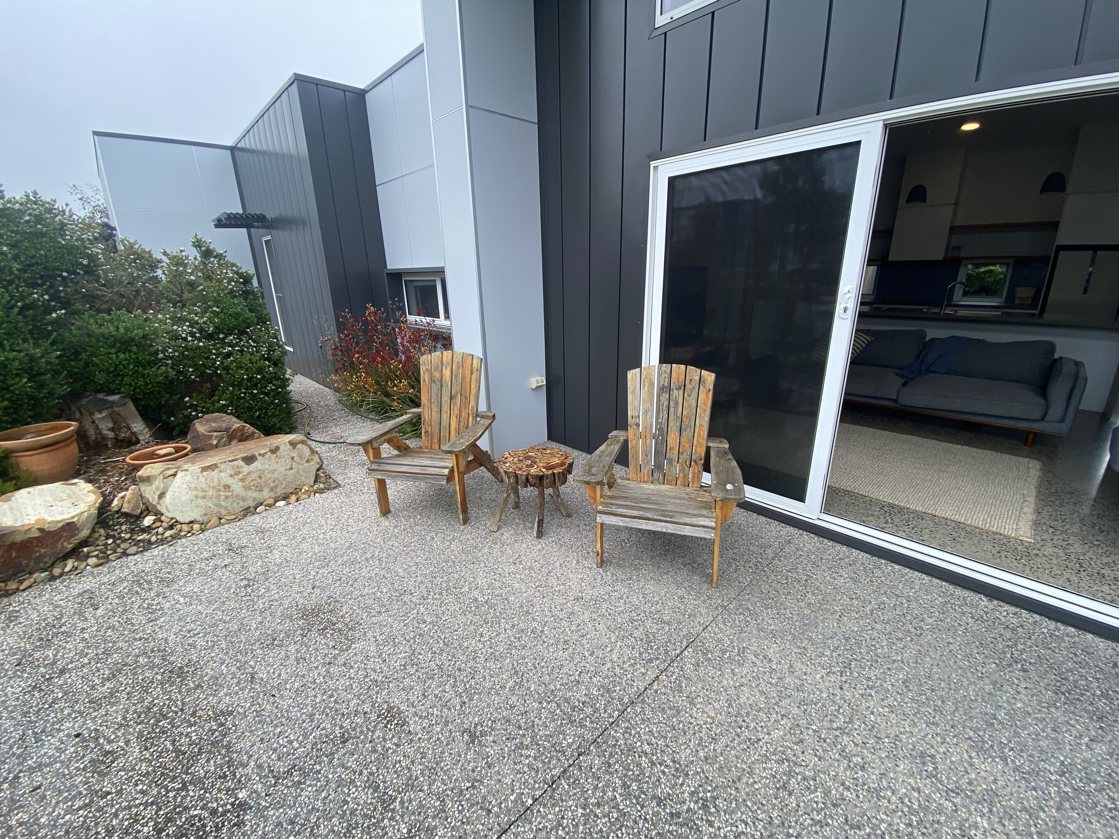 En uteplats med två trästolar i Adirondack-stil, ett litet runt bord och en stor krukväxt.