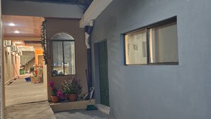 A narrow outdoor corridor with a small seating area, a potted plant, and a window with a view. - Milo's Hostel and Residences  (Santa Ana)