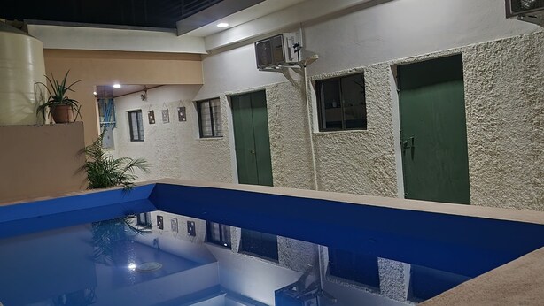 A swimming pool with a blue interior, surrounded by walls with textured white and beige surfaces, and green doors. - Milo's Hostel and Residences  (Santa Ana)