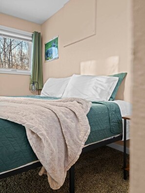 Un lit simple avec une couette verte et blanche, une couverture beige et une tête de lit.