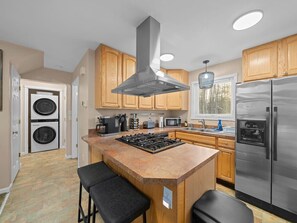 Una cocina moderna con gabinetes de madera, un refrigerador de acero inoxidable, horno empotrado, estufa a gas y una lavadora en la habitación contigua.