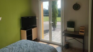Een slaapkamer met een bed, een televisie, een bureau en een glazen schuifdeur die uitkomt op een terras.