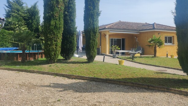 Een woonhuis met een gele gevel, een terras met tafel en stoelen, en een zwembad.