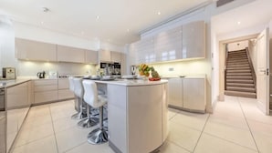 A modern kitchen with a central island, bar stools, and a staircase leading to an upper level. - Royal Mayfair Villa (London)