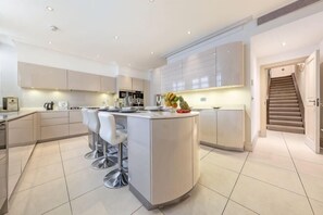 A modern kitchen with a central island, bar stools, and a staircase leading to an upper level. - Royal Mayfair Villa (London)