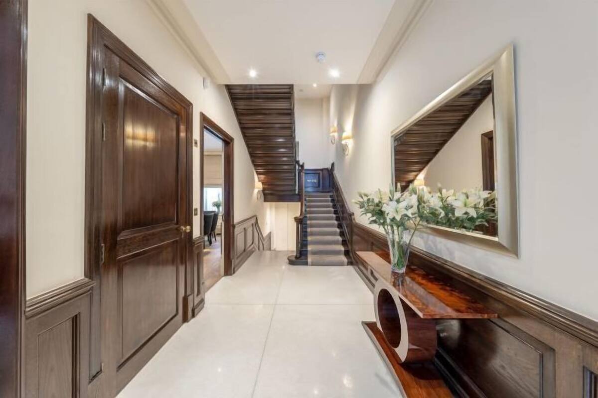 A hallway with a wooden door, a staircase, and a console table with a vase.