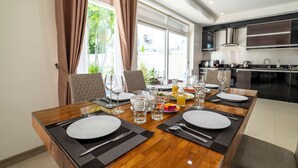 Una mesa de comedor dispuesta con platos, cubiertos y vasos, con una cocina al fondo.