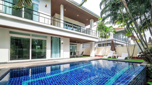 Una casa moderna de dos pisos con piscina, ventanas amplias y balcón.