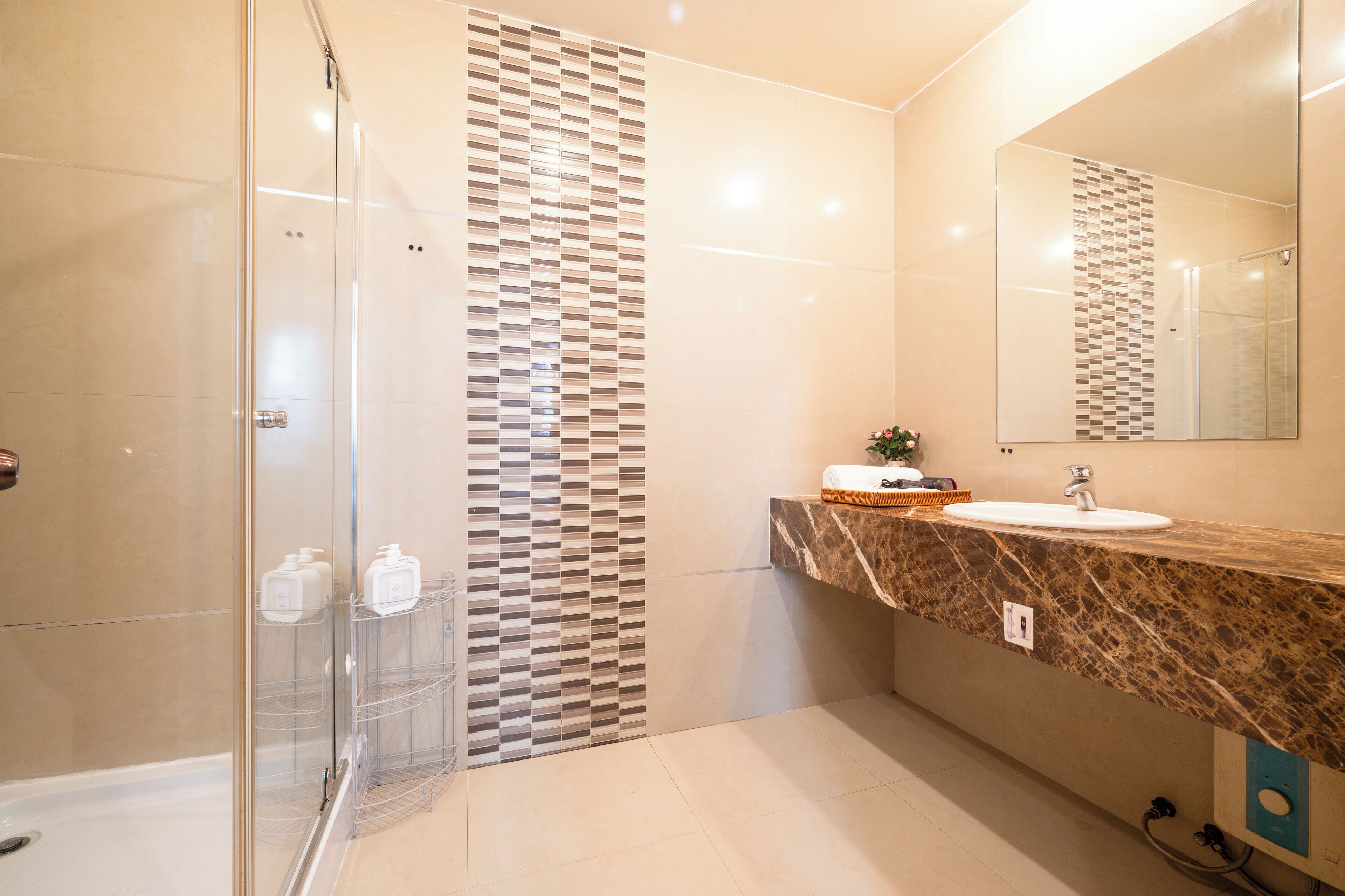 A modern bathroom with a glass shower enclosure, a marble countertop, and a large mirror.