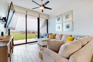 A modern living room with a large sofa, a flat-screen TV, and a ceiling fan. - High-End 2BR, Resort Perks: Suntide III - Unit 107 (South Padre Island)