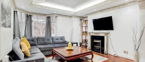 A living room with a sectional sofa, a coffee table, a fireplace, and a flat-screen TV mounted on the wall.