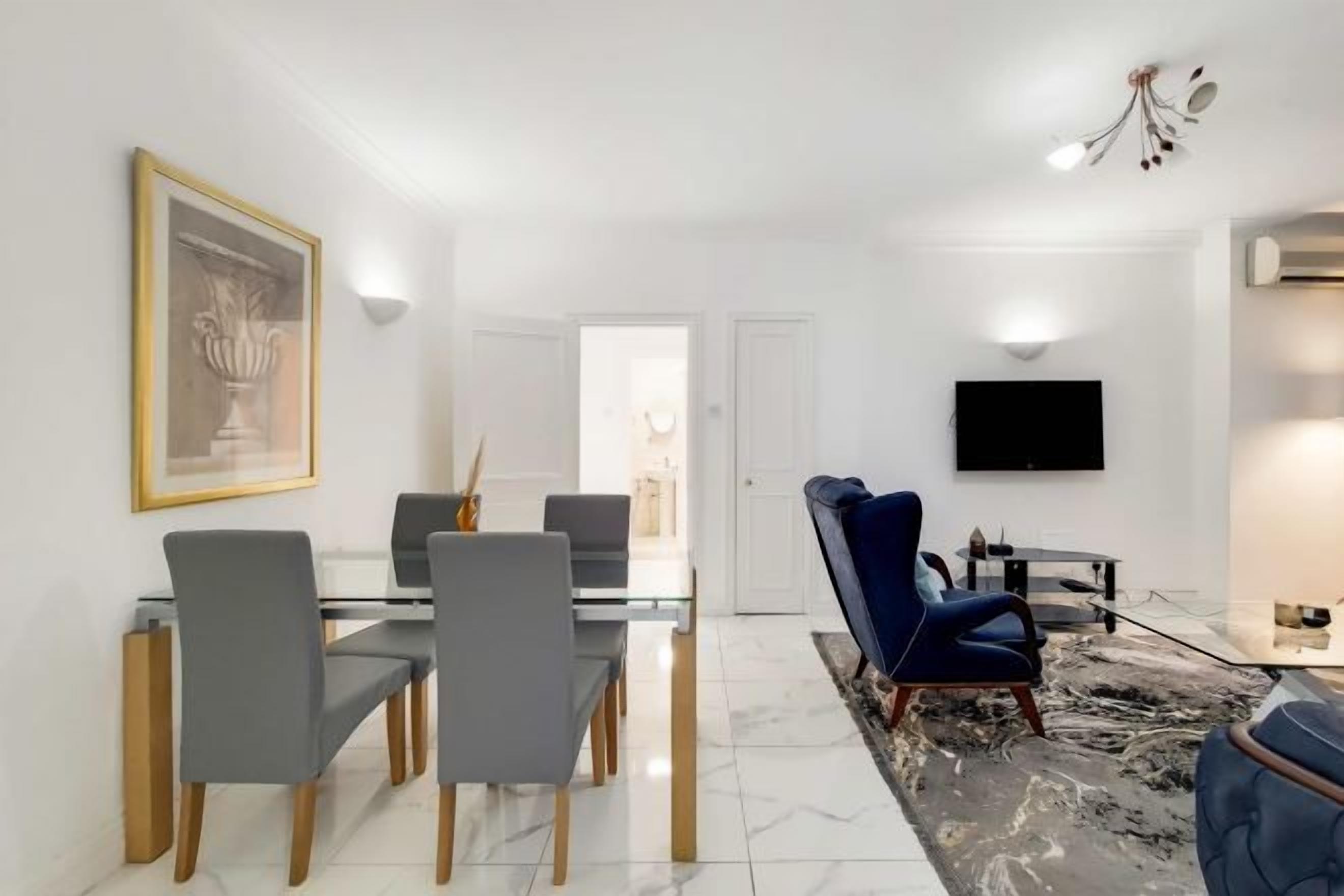 Un soggiorno moderno con zona pranzo, un divano blu, una TV a schermo piatto e un'opera d'arte incorniciata al muro.