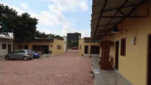 Un patio con un camino empedrado, una zona cubierta con estructura de madera y un coche rojo estacionado a lo lejos.