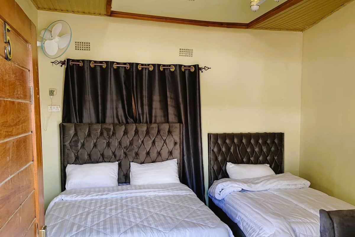 A bedroom with two beds, dark curtains, a ceiling fan, and a wooden door.