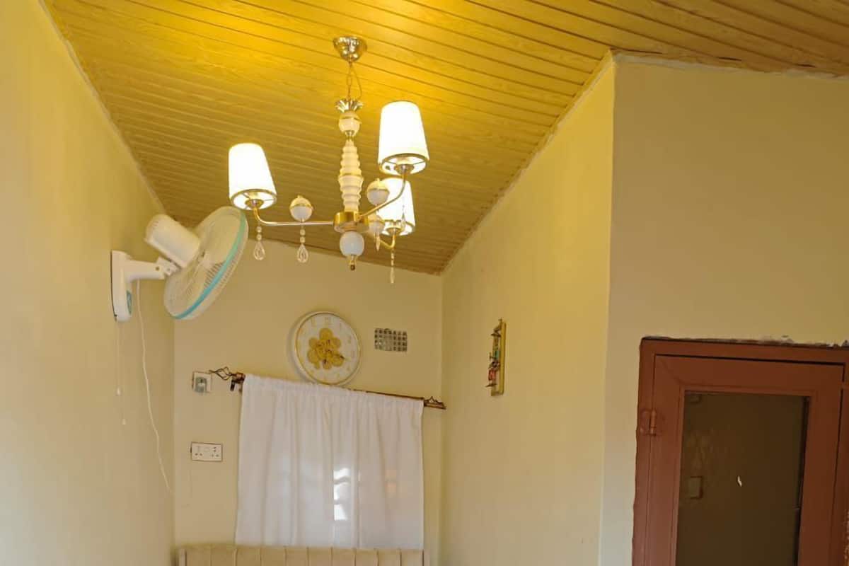 A single bed with a headboard, a ceiling fan, a wall clock, and a door to the right.