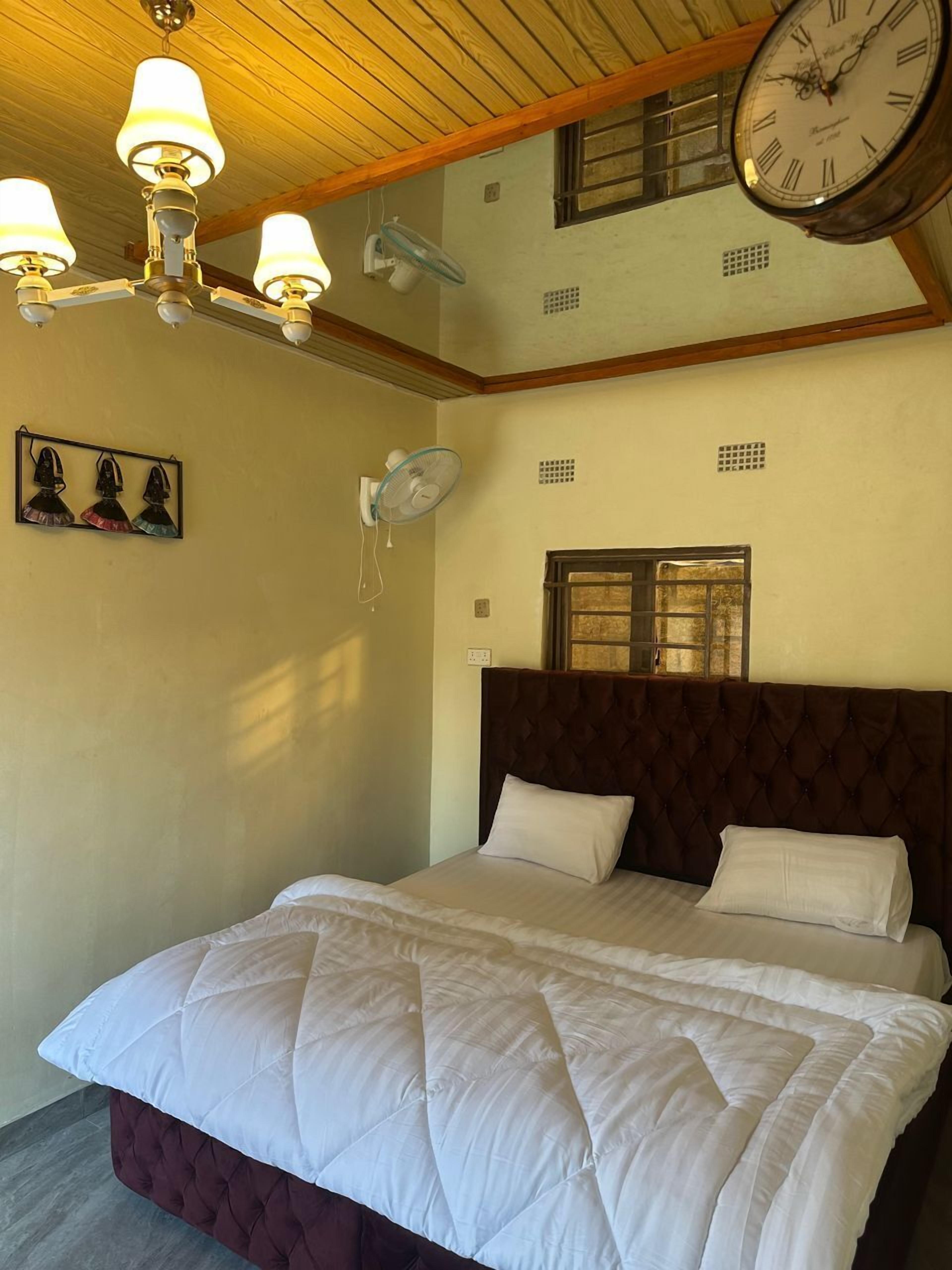 Un dormitorio con una cama grande, techo de madera, un reloj de pared y una ventana con contraventanas.